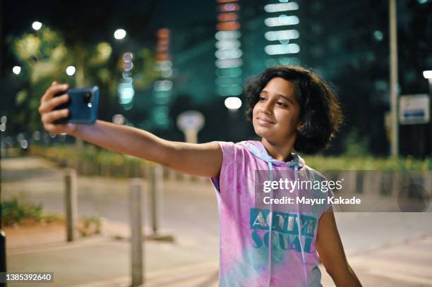 teenage girl taking selfie standing on a city street at night - 12 year old indian girl stock pictures, royalty-free photos & images