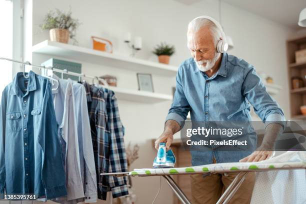 senior mann hört musik beim bügeln - bügeleisen stock-fotos und bilder