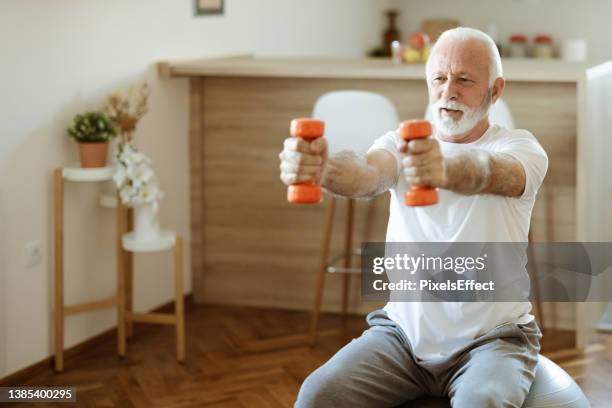 senior man siting on fit ball doing exercise with dumbbell - treino de força imagens e fotografias de stock