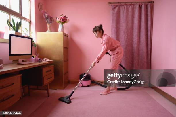 mature woman vacuuming carpet in pink home office - pink color stockfoto's en -beelden