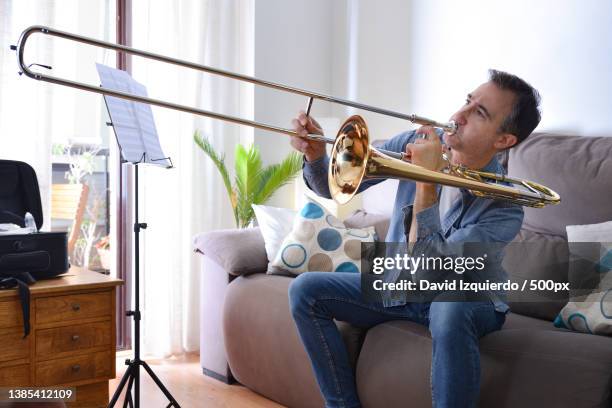 novice man playing trombone at home with enthusiasm - trombone stock pictures, royalty-free photos & images