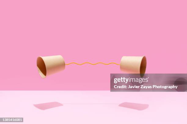 two paper cups united with a yellow string on a pink background - language and communication ストックフォトと画像