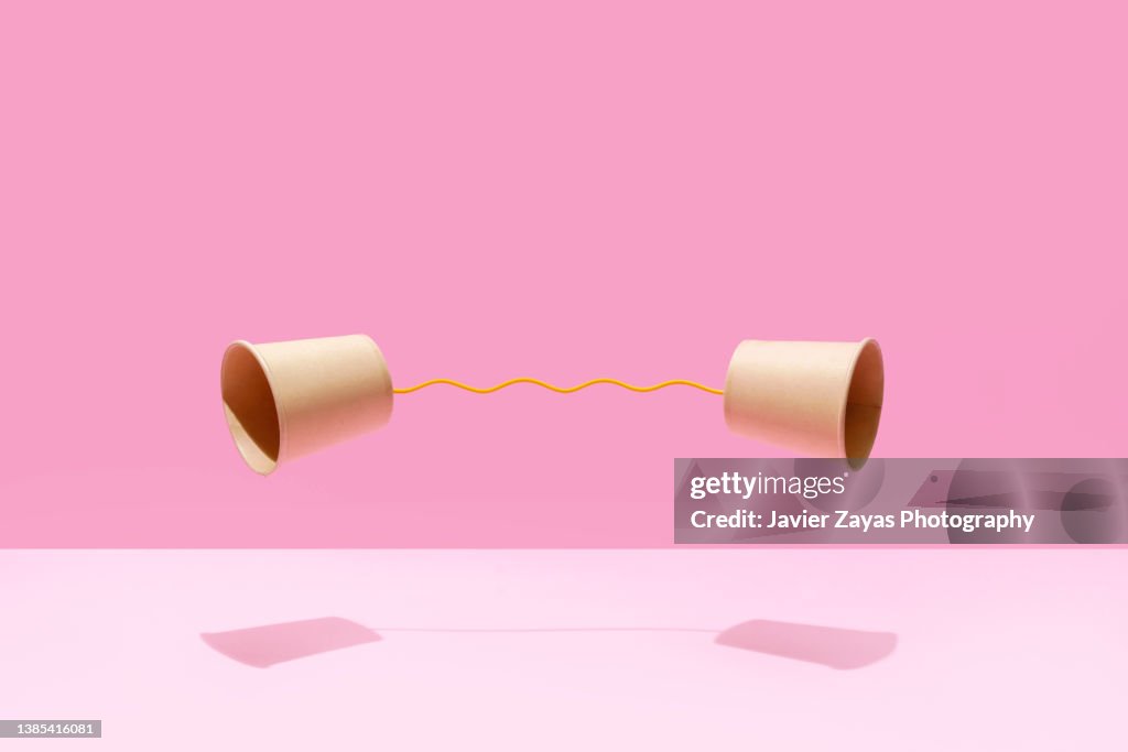 Two Paper Cups United With A Yellow String On A Pink Background