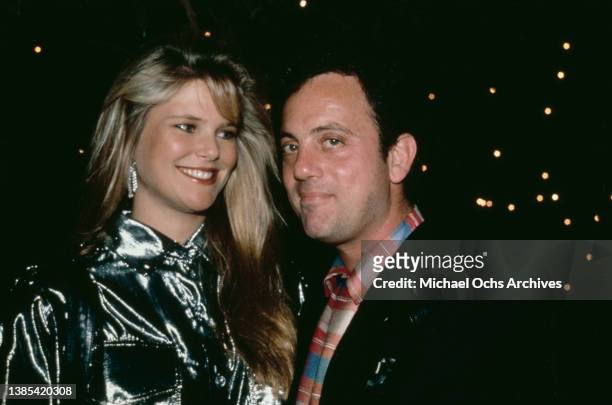 American model Christie Brinkley, wearing a silver jacket, and her husband, American singer-songwriter and musician Billy Joel. Wearing a checked...