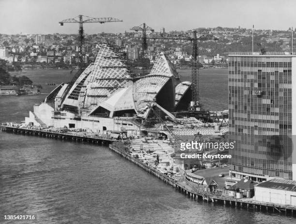 Cranes rise above the shell-like structures of the roof of Sydney Opera House under construction on the site of a former tram shed, on Bennelong...