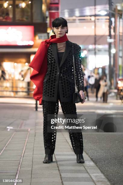 Guest is seen wearing black cut-out pattern design outfit with red scarf outside Shibuya Hikarie during Rakuten Fashion Week Tokyo 2022 A/W on March...