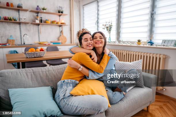 two female friends embracing each other - 2 young woman on couch stock pictures, royalty-free photos & images