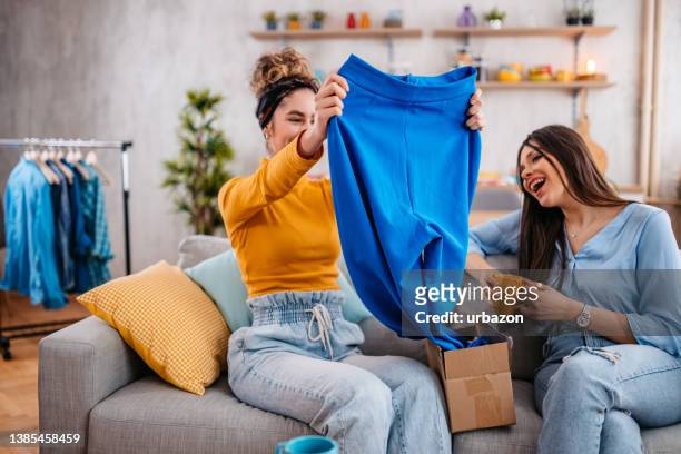 young woman showing her female friend the pants she ordered online - system demonstration stock pictures, royalty-free photos & images