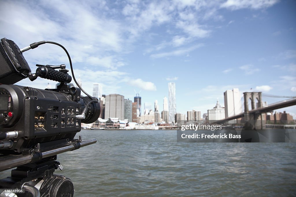 A television camera filming the Brooklyn Bridge and Manhattan skyline