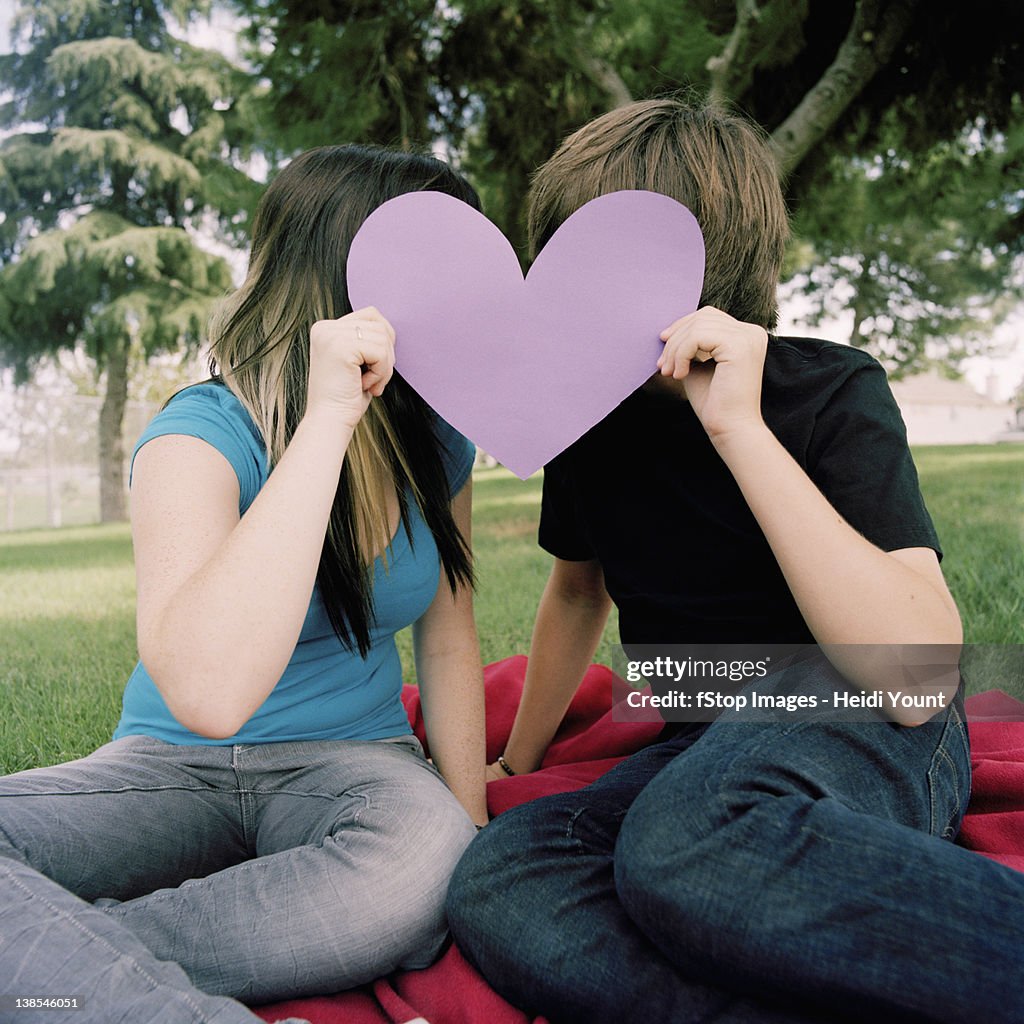 A teenage couple hiding behind a cut out heart