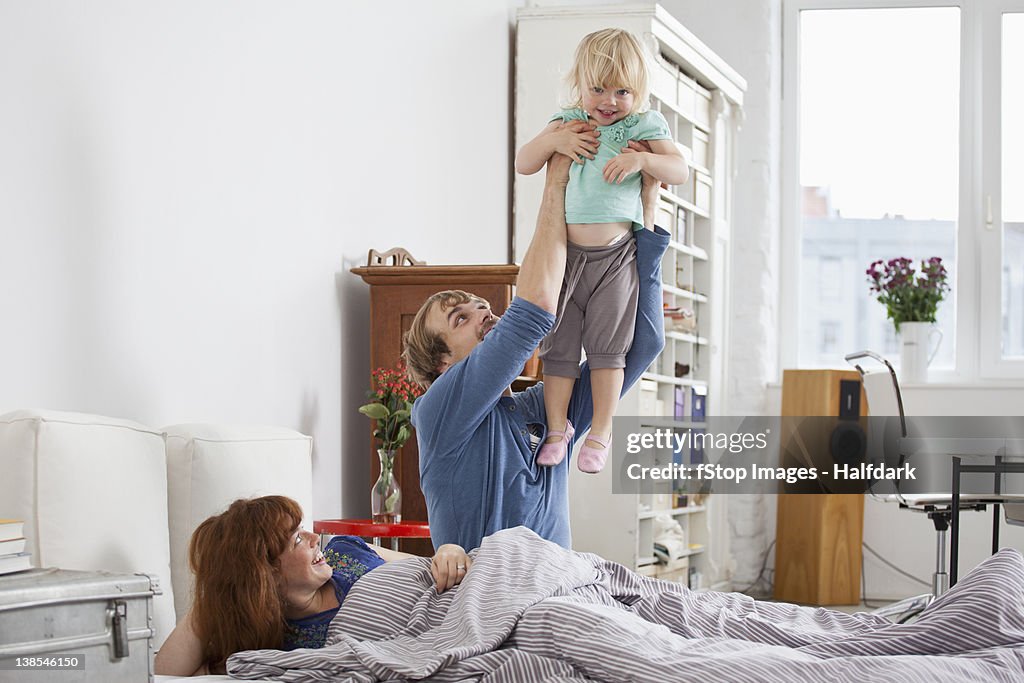 A couple in bed, man holding daughter aloft