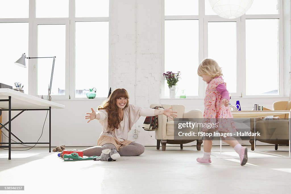 A young girl running towards her mother sitting on the floor