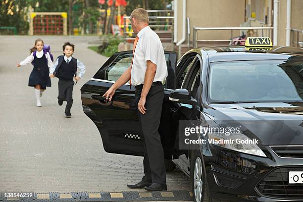 two children in school uniforms running towards black cab - chauffeur stock pictures, royalty-free photos & images