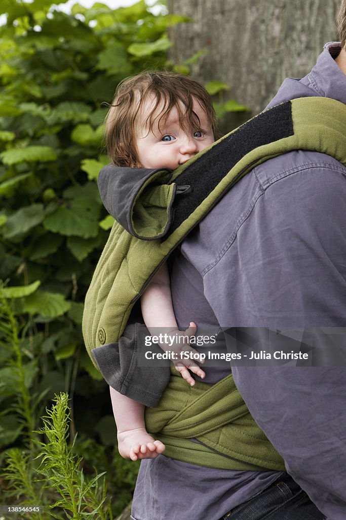 A father carrying his baby daughter in baby carrier, focus on baby