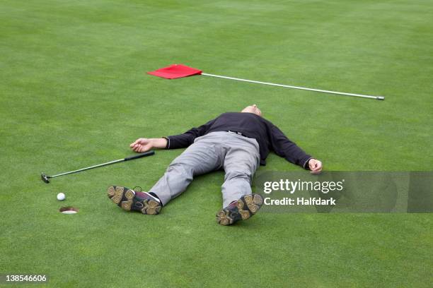 a distraught golfer lying on putting green with ball at the edge of hole - putting golf stock pictures, royalty-free photos & images