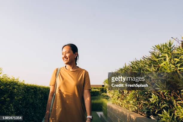 belle femme asiatique en robe jaune décontractée marchant dans le parc par une journée ensoleillée - robe jaune photos et images de collection