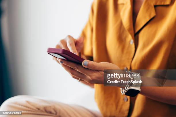 mujer asiática anónima con una camisa amarilla sentada en la cama del hotel y navegando por la web en su teléfono inteligente - yellow shirt fotografías e imágenes de stock