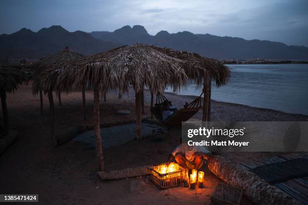 Man relaxes in a hammock while a worker distributes candles at camp Ras Shitan during the Passover holiday on April 25, 2008 near the city of Nuweiba...