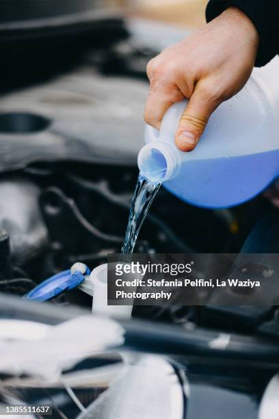 hand pouring windshield washer cleaner in an automobile's tank - vorratstank stock-fotos und bilder