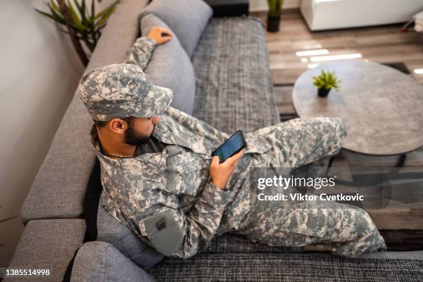 soldado sentado en el sofá de la sala de estar y usando un teléfono inteligente - ranking fotografías e imágenes de stock