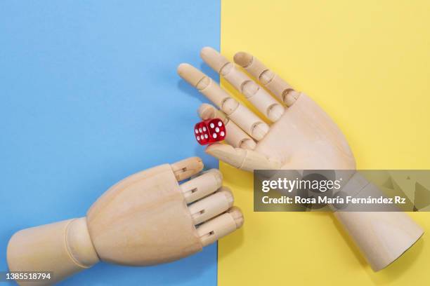 wooden figurine hands one of them with a red  dice on  blue and yellow background.  russia and ukraine conflict concept. russian ukrainian war. - mannequin arm stock pictures, royalty-free photos & images