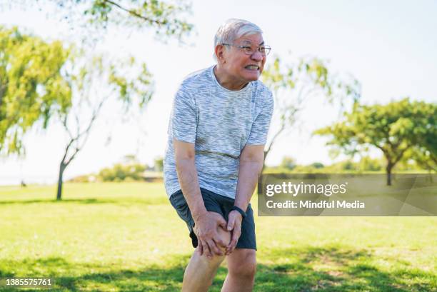 asiatisch-amerikanischer reifer mann, der mit den händen knie hält und unter schmerzen leidet - sehnenscheidenentzündung stock-fotos und bilder