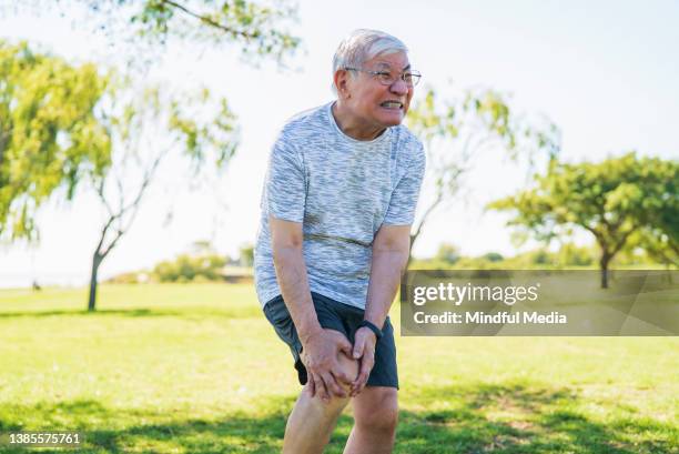 asian american mature man holding knee with hands and suffering with pain - meniscus stock pictures, royalty-free photos & images