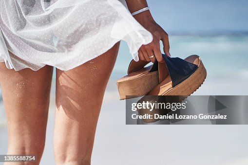 Woman with sandals in hand on sandy seashore Woman with sandals in hand on sandy seashore