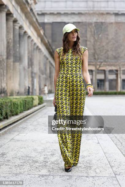 Influencer Anna Verkhorubova wearing a yellow camouflage print jumpsuit by Natascha Gruen, a pastel yellow cap by Y-3, a black bag with gold studs by...