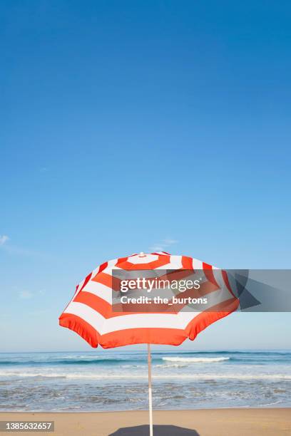 striped parasol on the beach against blue sky - strandschirm stock-fotos und bilder