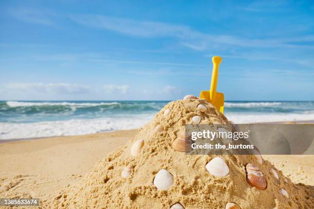 still life of sand castle and yellow shovel at sea against blue sky - sand castle bildbanksfoton och bilder