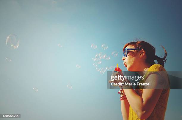 girl blowing bubbles into blue sky - bubble wand photos et images de collection