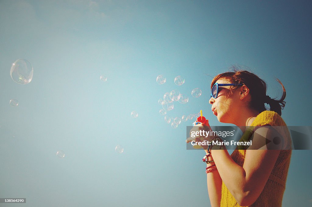 Girl blowing bubbles into blue sky