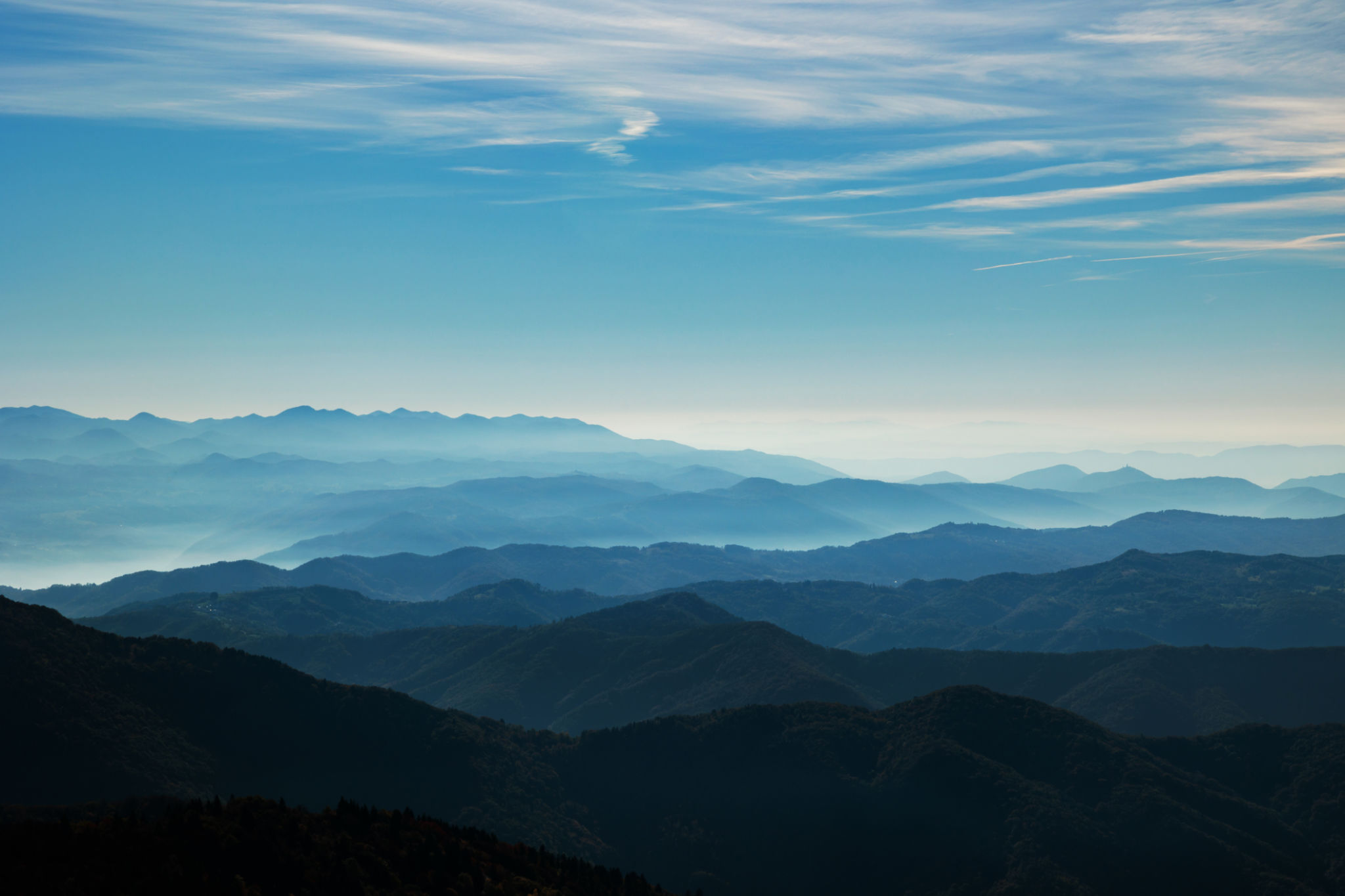 beautiful hills and mountains, colored of shades of blue, extending up to the horizon at daytime, while being lit by the sunlight, bright fog passing through the valleys, light blue sky filled with various thin little clouds beautiful hills and mountains, colored of shades of blue, extending up to the horizon at daytime, while being lit by the sunlight, bright fog passing through the valleys, light blue sky filled with various thin little clouds