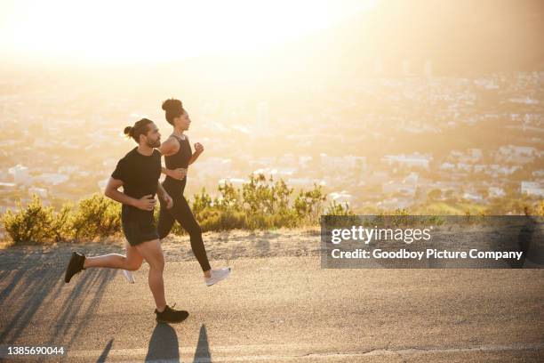 two fit young people jogging together along a scenic road - fitness couple stockfoto's en -beelden