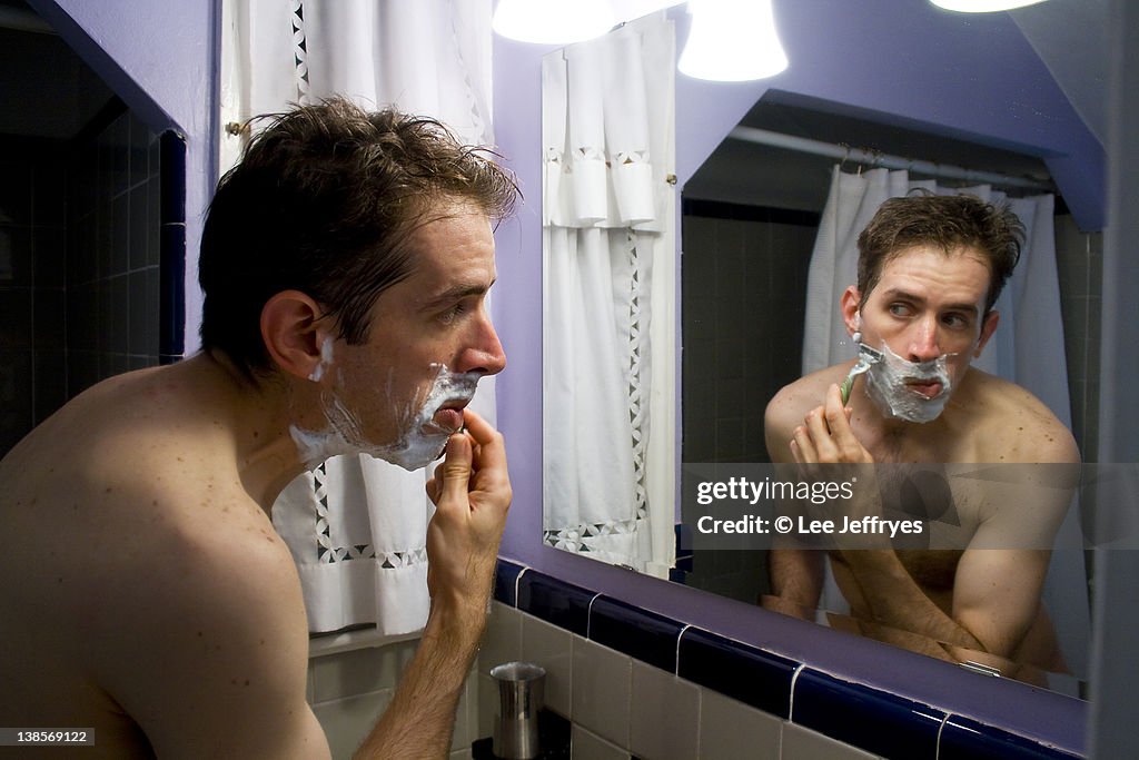 Man shaving in bathroom mirror