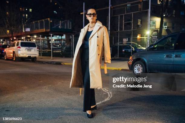 Model and Interview Magazine Fashion Director Dara Allen wears a tan trench, sunglasses, chunky gold earrings and necklace, black top, black pants,...