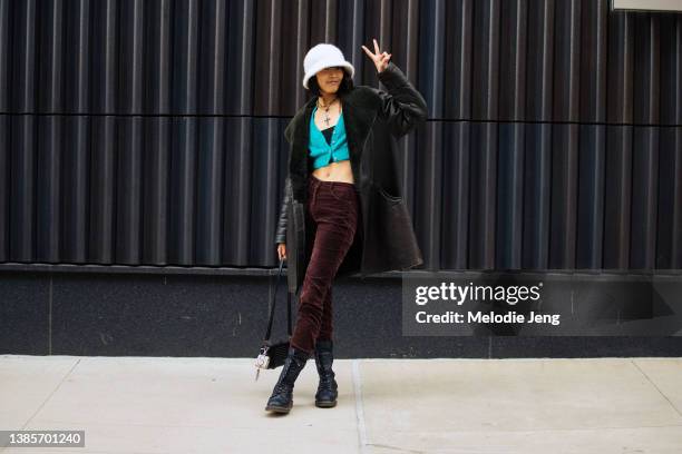 Japanese model Amane Taniguchi throws a peace sign and wears a white fuzzy bucket hat, black shearling jacket, aqua cropped fuzzy cardigan, black...