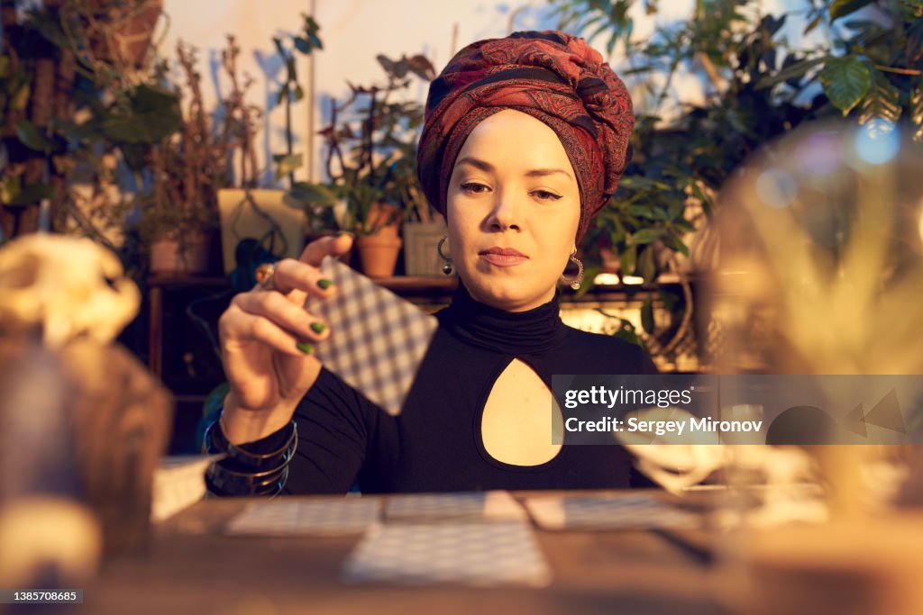Female enchantress spreading tarot cards at table