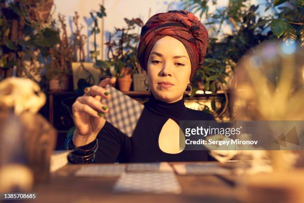 female enchantress spreading tarot cards at table - fortune teller fotografías e imágenes de stock