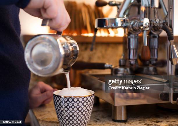 man pouring frothy milk in coffee mug - milchschaum stock-fotos und bilder