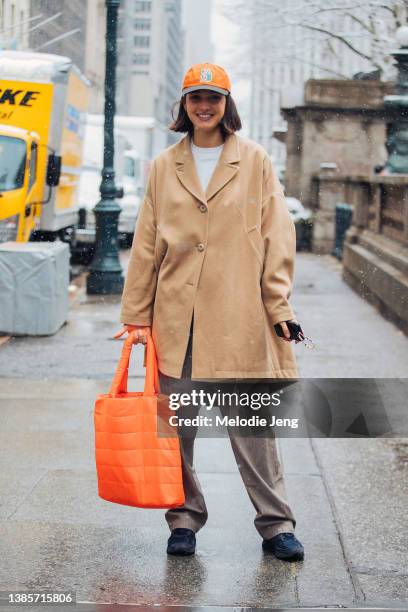 Canadian model Rachelle Harris wears an orange Stussy cap, tan flare vintage Margiela coat, orange Fuel Ultra-lite Tote down bag, gray pants, black...