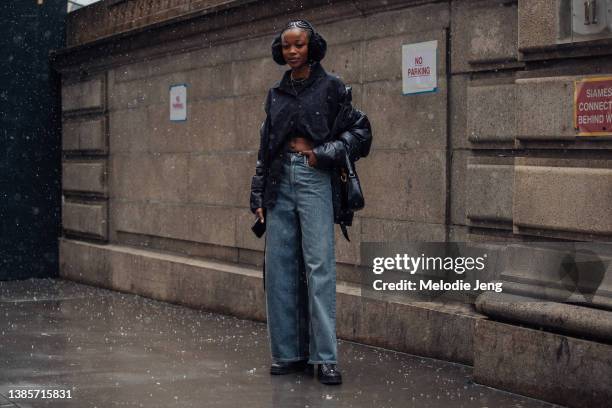 Nigerian model Precious Kevin wears earmuffs, a black puffer jacket off her shoulders, black blousem, blue jeans, black purse, and black boots after...
