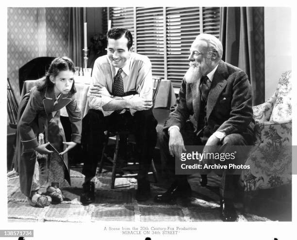 Edmund Gwenn and unknown actor sitting in a chair laughing when a child is making funny gestures in a scene from the film 'Miracle On 34th Street',...