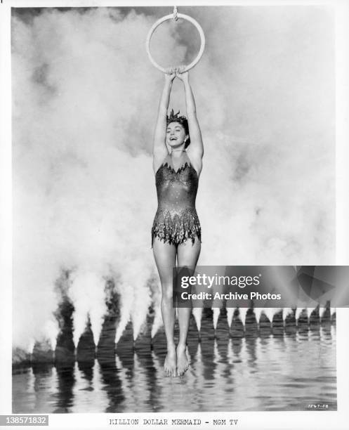 Esther William holding onto a ring and swinging precisionly above smokey water in a scene from the film 'Million Dollar Mermaid', 1952.