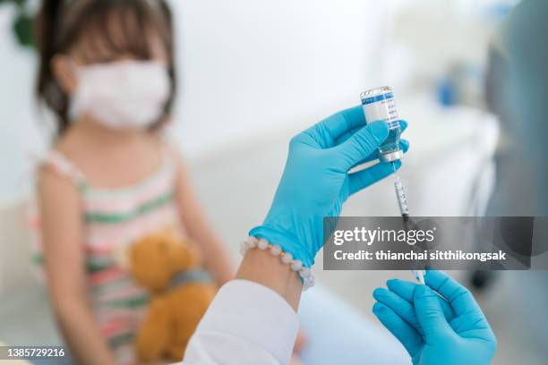 close-up of doctor with a syringe and sweet blond girl holding teddy bear on background - covid 19 vaccine stock pictures, royalty-free photos & images