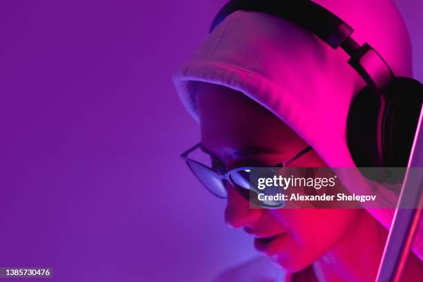 weibliches porträt im neonlicht. modefrau in lila farbe. lebendiger hintergrund im studio. futuristisches konzept. mädchen tragen sonnenbrille und kapuzenpullover und hören musik in drahtlosen kopfhörern - fluorescent stock-fotos und bilder