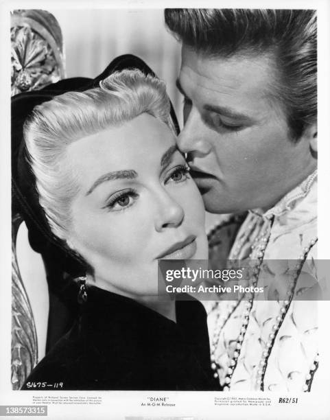 Lana Turner stares forward as Roger Moore seductively kisses her cheek in a scene from the film 'Diane', 1956.