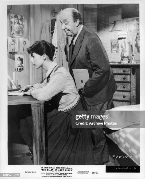 Millie Perkins sits at a desk facing a wall and Joseph Schildkraut stands behind her in a scene from the film 'The Diary Of Anne Frank', 1959.