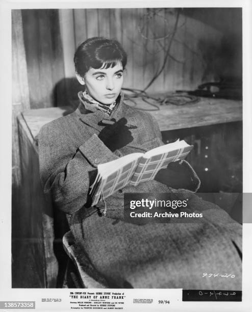 Millie Perkins sitting wearing a coat and gloves holding a journal with a pen in her hand in a scene from the film 'The Diary Of Anne Frank', 1959.